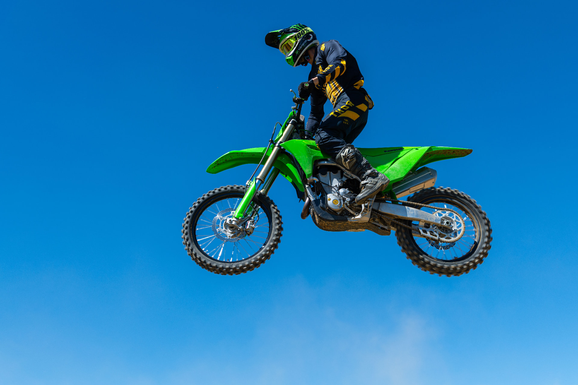 Motocross rider jumping a green dirt bike against a blue sky
